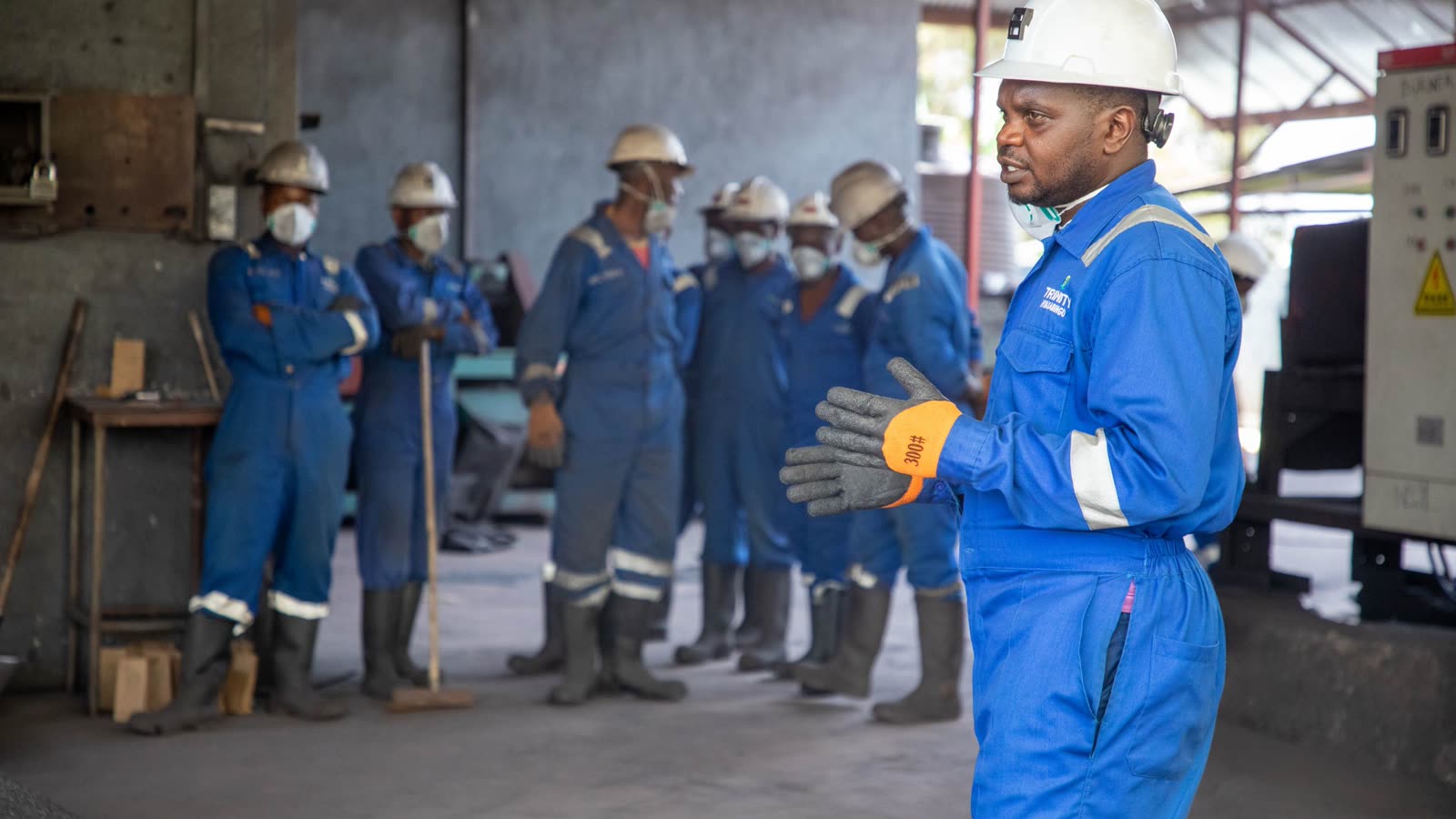 A trainer briefing a group of artisans in coveralls and hard hats at a training session