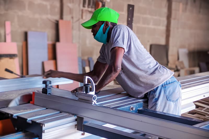 A carpenter feeding a board through a panel saw in a workshop