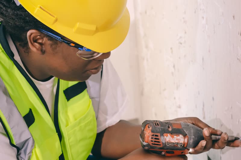 An electrician drilling into a wall beside a socket