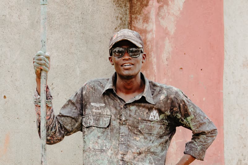 A painter in paint-spattered workwear standing against a rendered wall